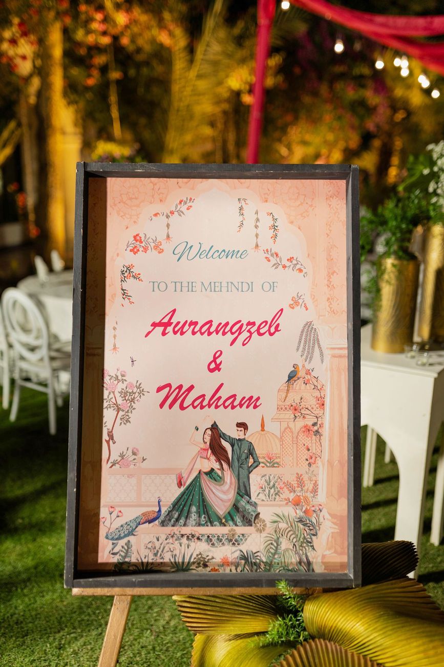 Welcome sign for the mehndi of Aurangzeb and Maham, illustrated with a dancing couple, set among string lights, Maham & Aurangzeb's wedding