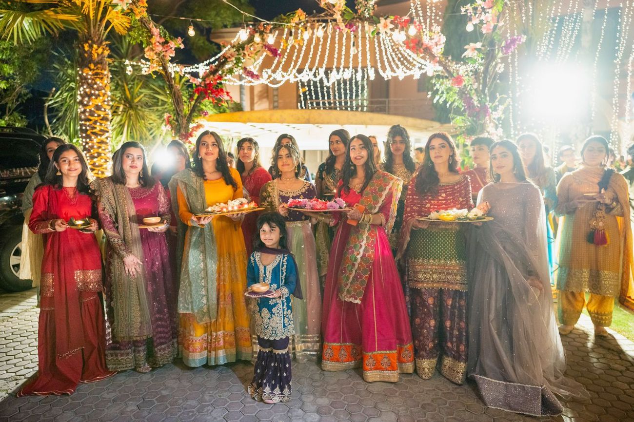 Group of women holding lit diyas on trays during the mehndi entrance procession, Maham & Aurangzeb's wedding