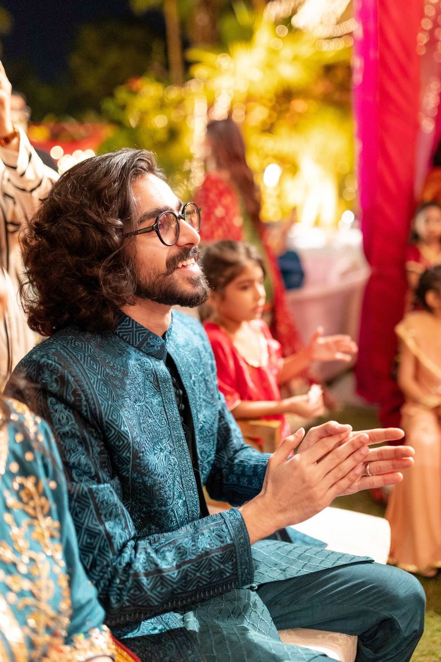 Groom clapping and smiling while seated at the mehndi celebration, Maham & Aurangzeb's wedding