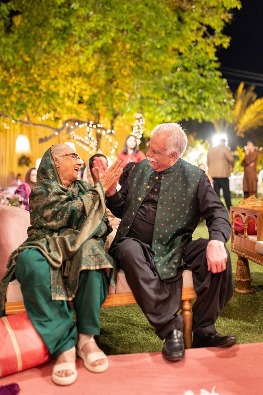 Older couple sharing a laugh and high-fiving at the mehndi celebration, Maham & Aurangzeb's wedding