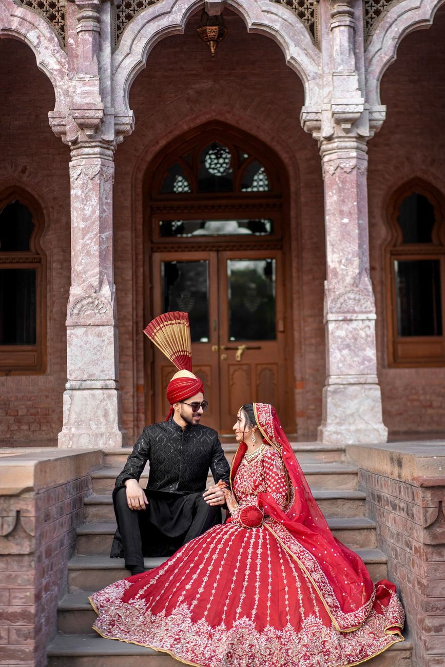 Bride and groom seated together on heritage steps beneath a Mughal-style brick archway, Maham & Aurangzeb's wedding at Aitchison College, Lahore