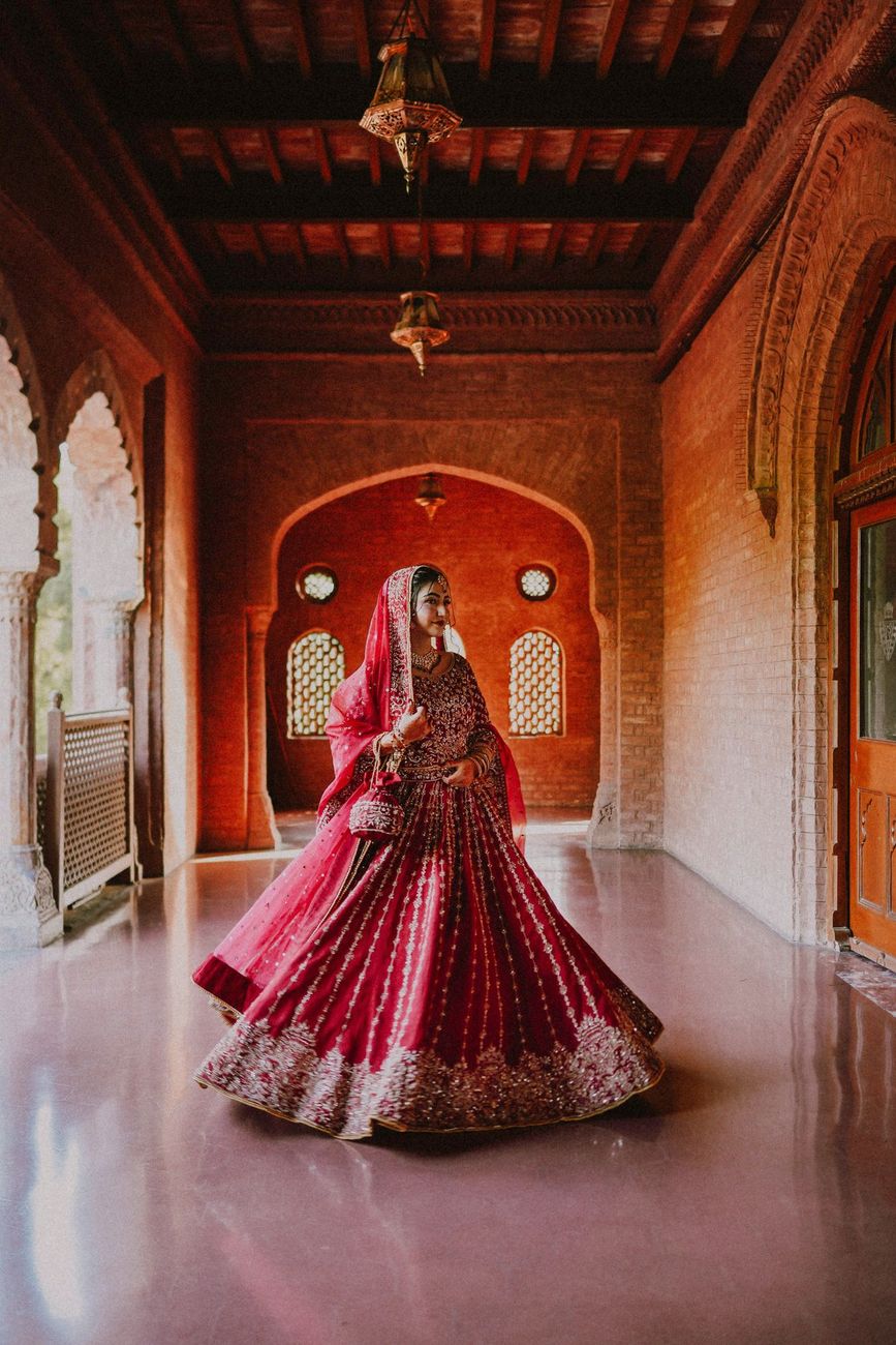 Solo bridal portrait twirling in a red lehenga down a heritage brick corridor, Maham & Aurangzeb's wedding at Aitchison College, Lahore