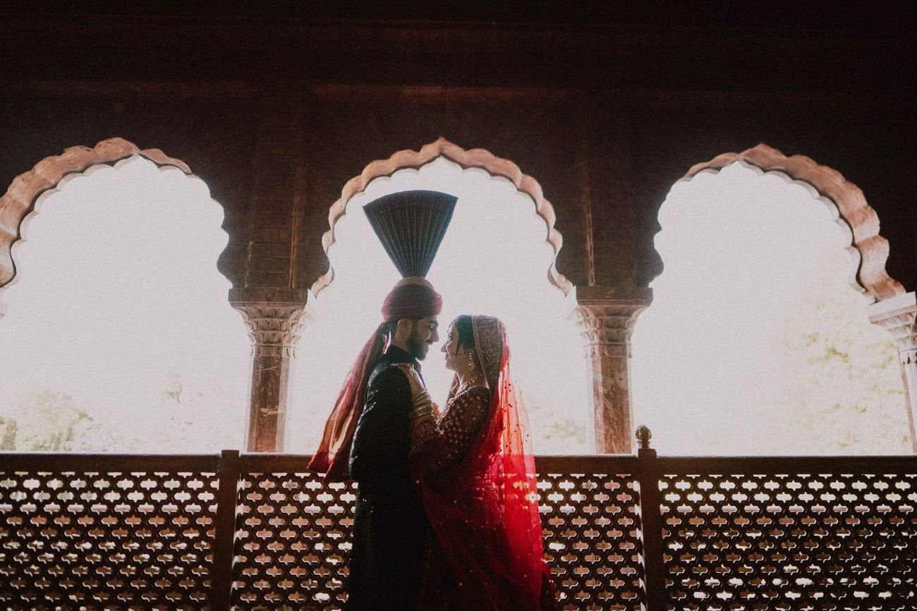 Silhouette of bride and groom embracing beneath ornate scalloped archways at golden hour, Maham & Aurangzeb's wedding at Aitchison College, Lahore