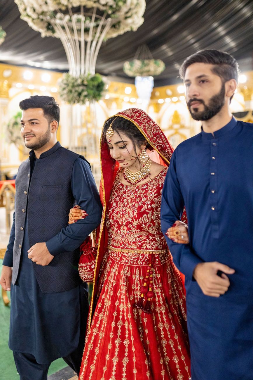 Bride being escorted between two family members at the reception, eyes closed, Maham & Aurangzeb's wedding