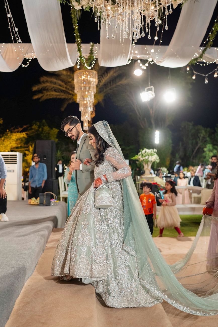 Bride in a sage green sequined gown with a long train walking into the walima reception with the groom, Maham & Aurangzeb's wedding