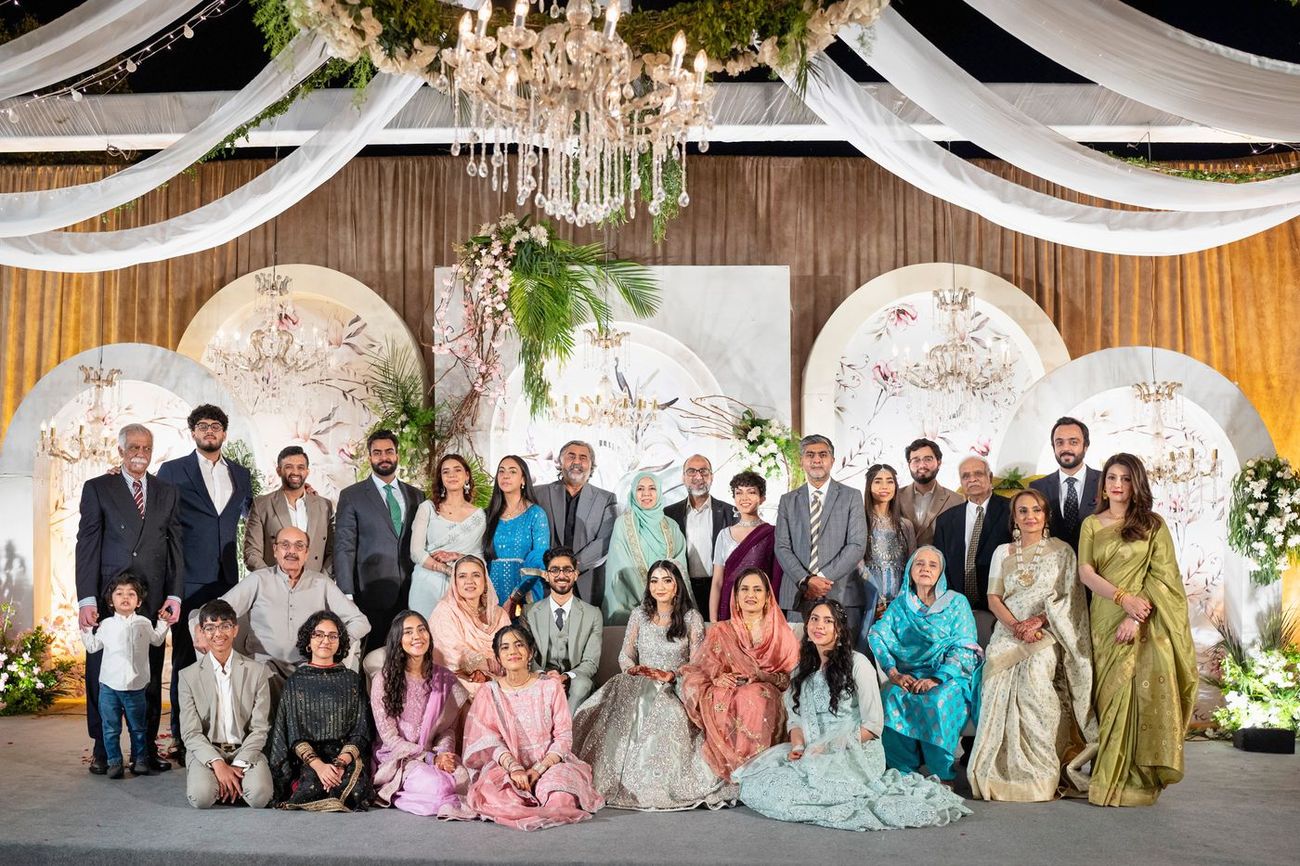 Large extended family group portrait at the walima reception, floral arched backdrop behind them, Maham & Aurangzeb's wedding