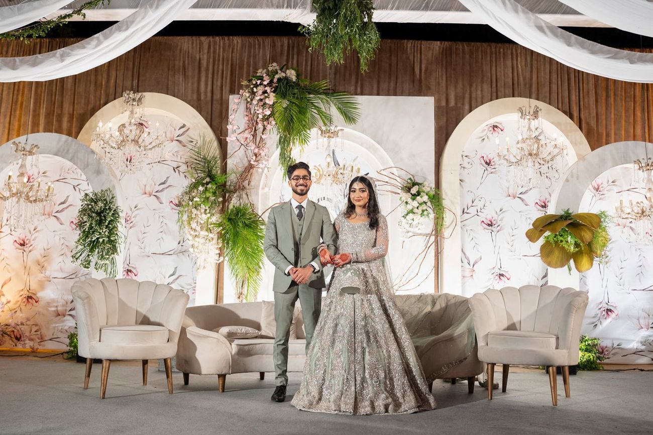 Bride and groom standing together on the walima stage in front of floral arched panels, Maham & Aurangzeb's wedding