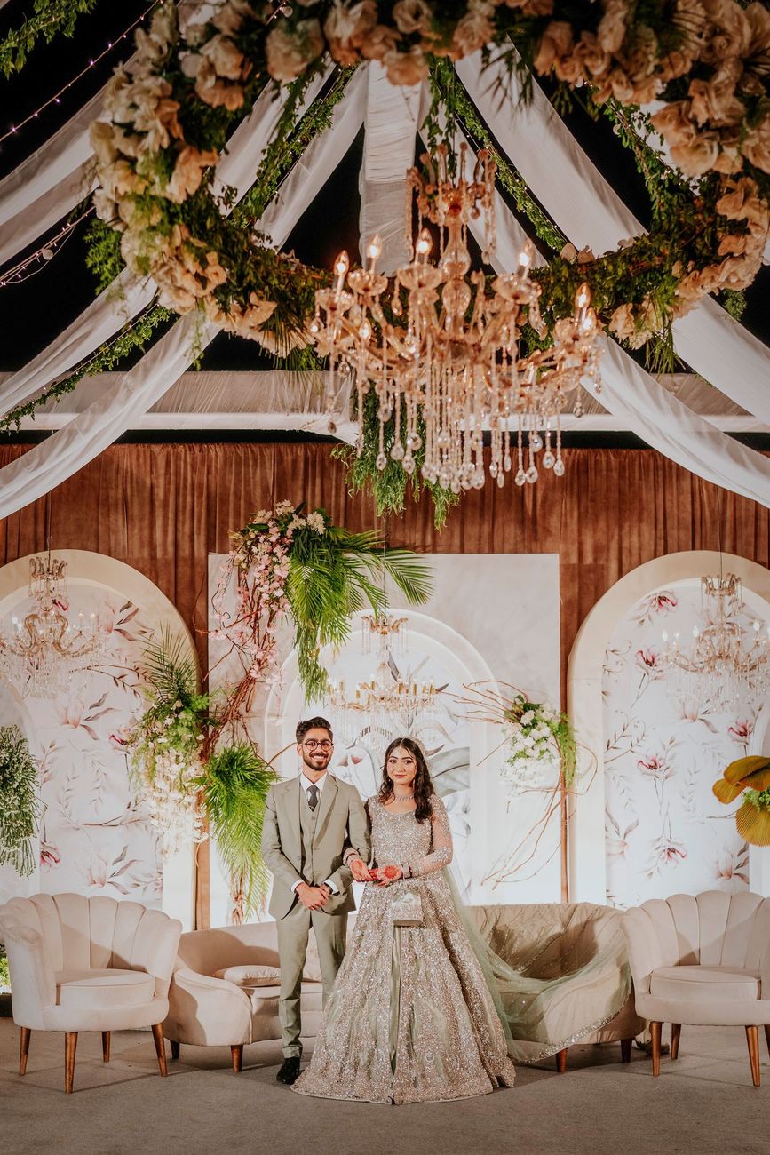 Bride and groom standing together on the walima stage beneath a floral chandelier, Maham & Aurangzeb's wedding