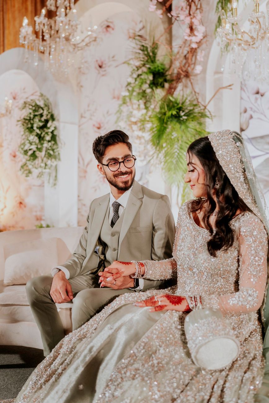 Bride and groom seated together on a sofa at the walima reception, smiling at each other, Maham & Aurangzeb's wedding
