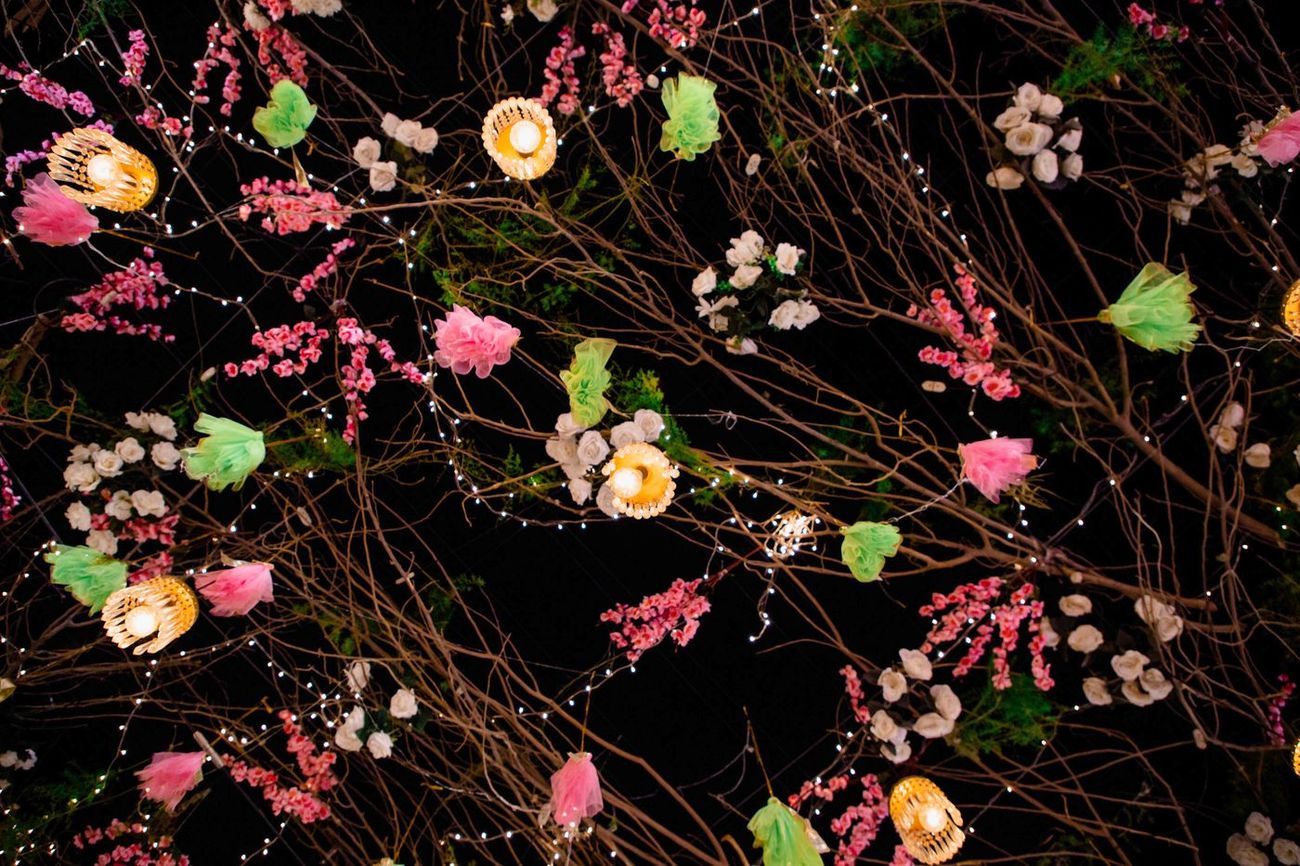 Detail of colorful tassels, fairy lights, and paper flowers hanging from branches, Mashal & Danial's mehndi