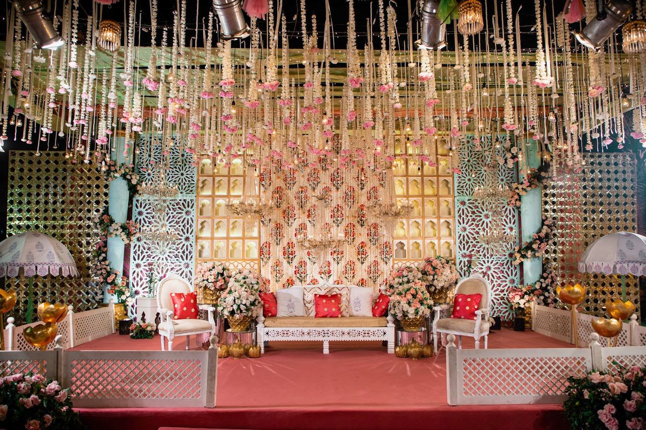 Wide shot of the empty mehndi stage with a floral arch backdrop and red cushioned seating, Mashal & Danial's wedding