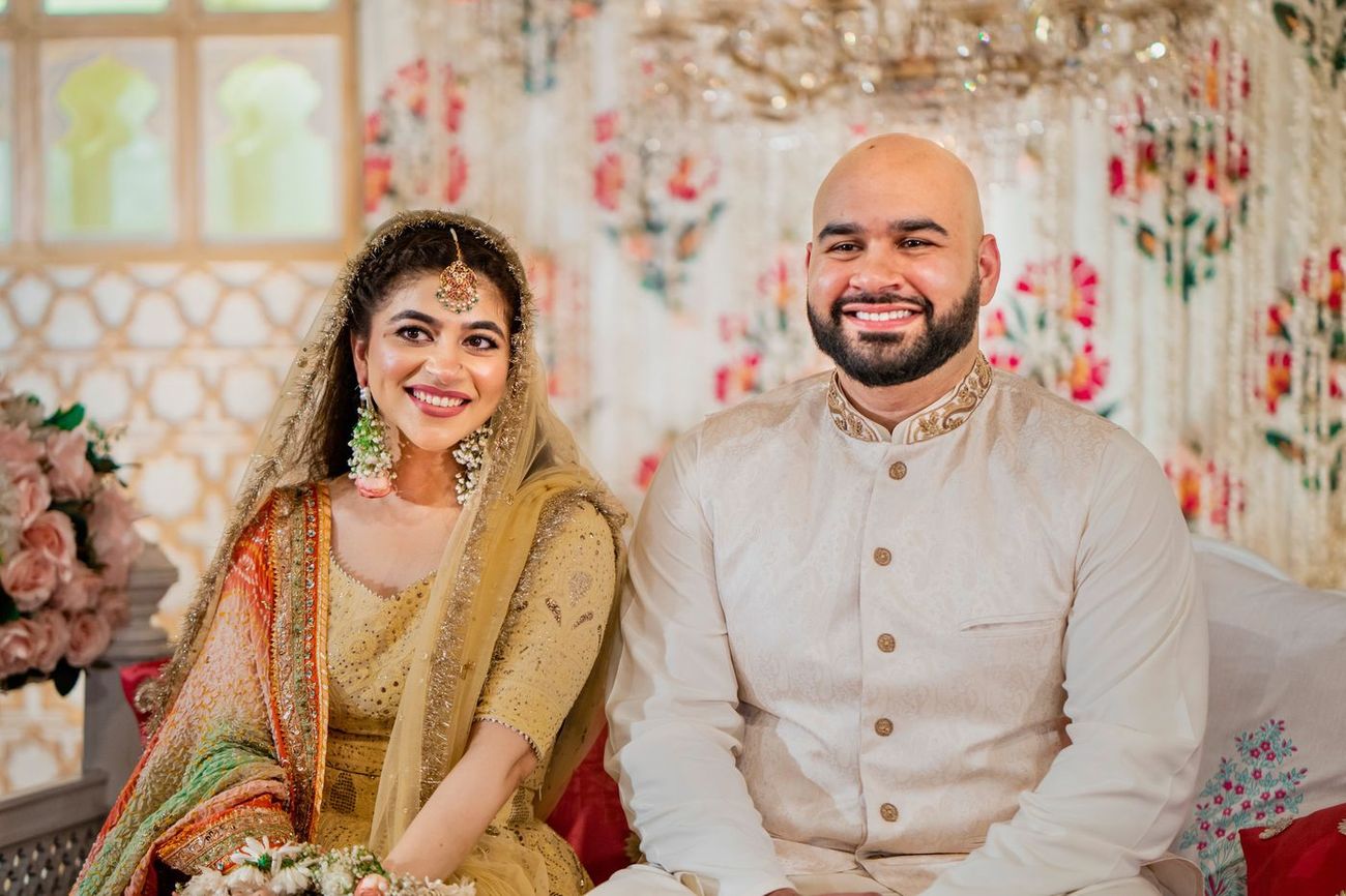 Bride and groom smiling together in matching yellow and cream mehndi outfits, floral arch behind them, Mashal & Danial's wedding