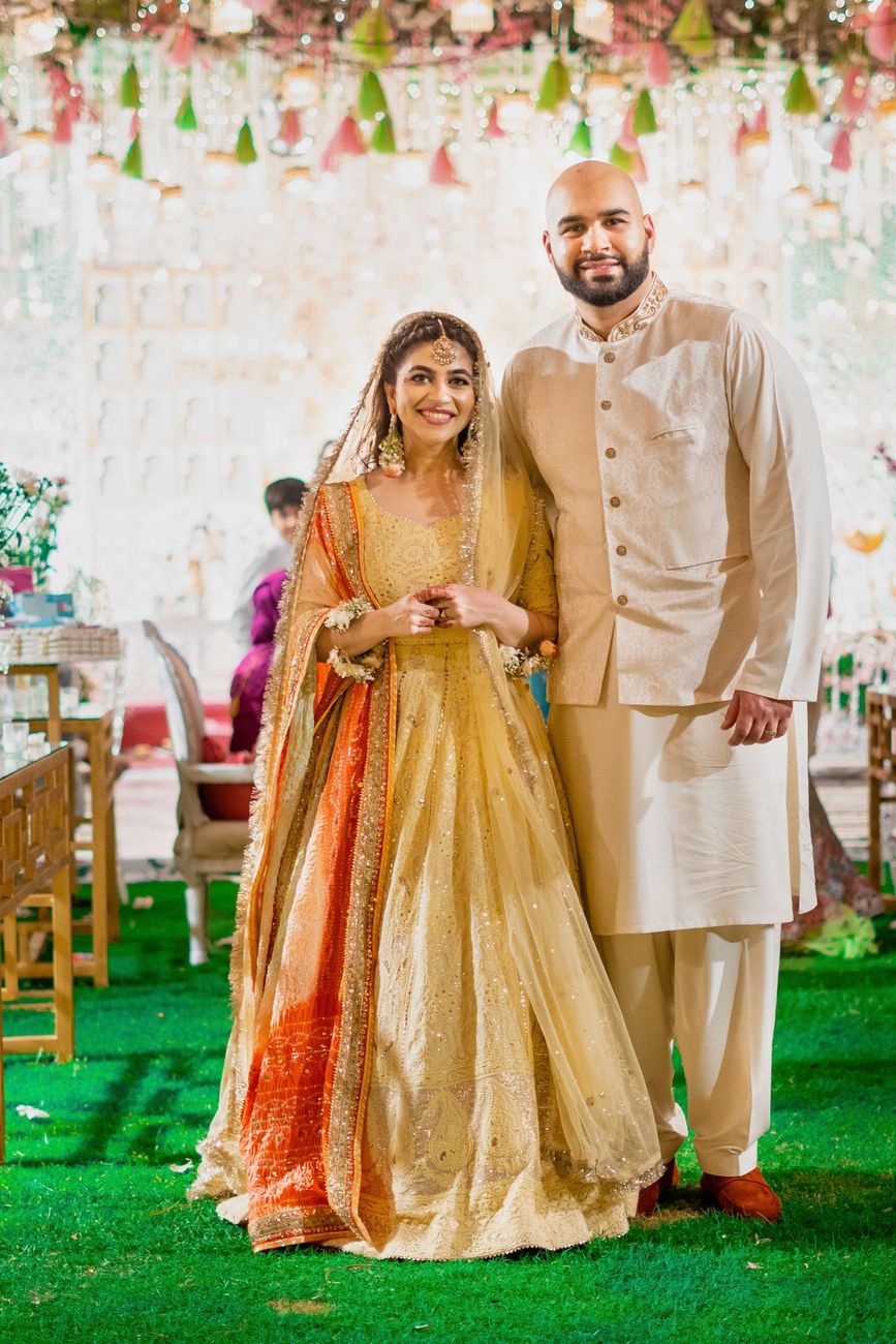 Bride and groom standing together on the lawn in matching yellow and cream mehndi outfits, Mashal & Danial's wedding