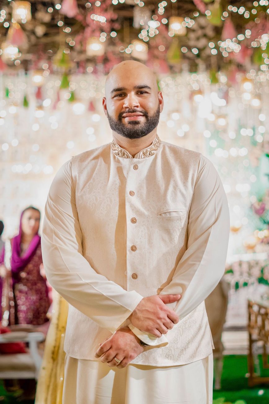 Solo groom portrait in a cream waistcoat beneath hanging mehndi lights, Mashal & Danial's wedding