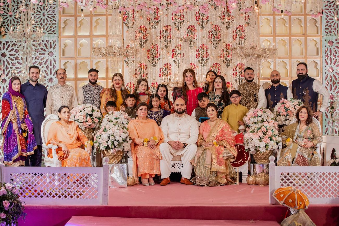 Large extended family group portrait on the mehndi stage with floral chandeliers above, Mashal & Danial's wedding