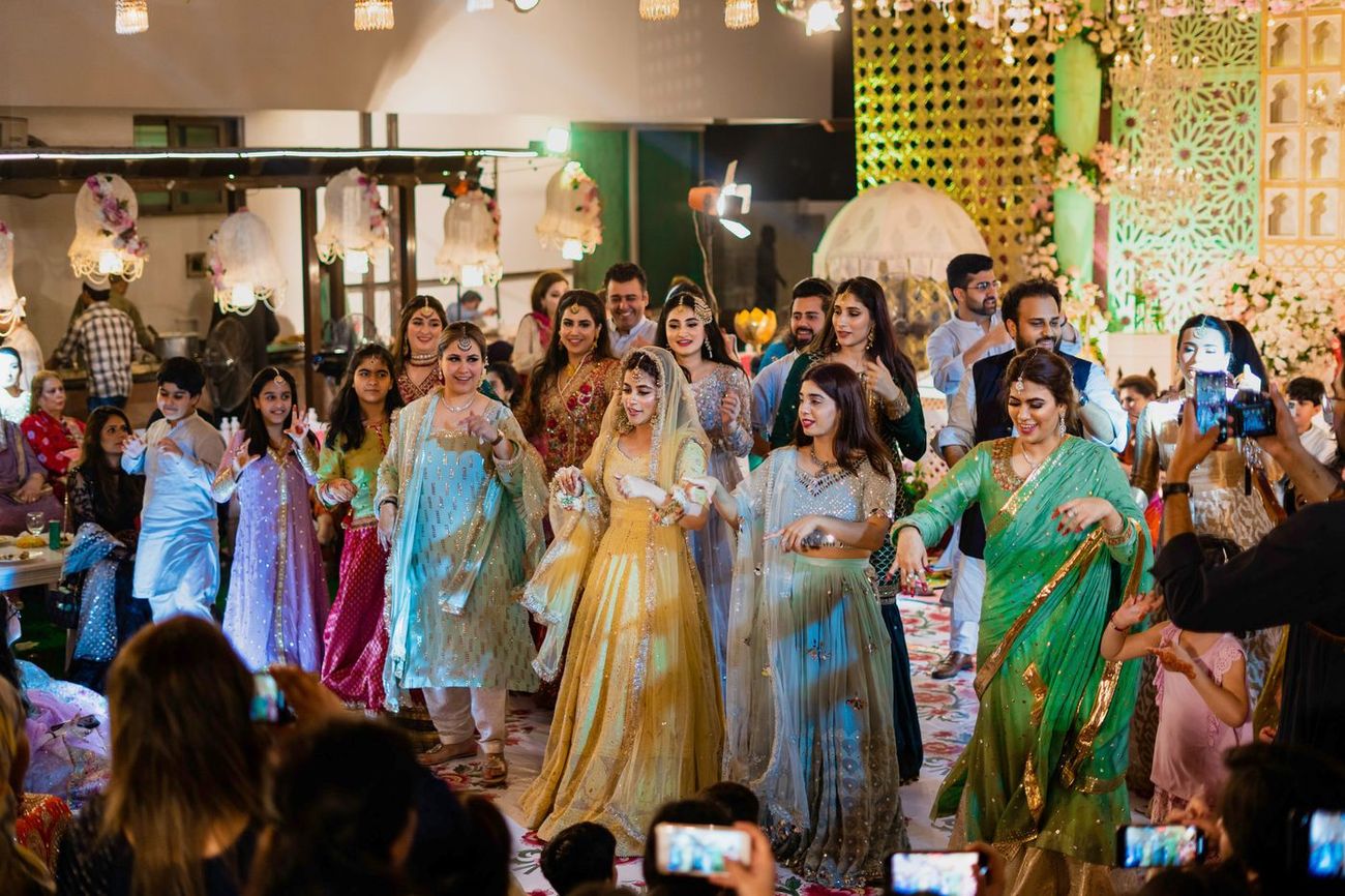 Group of women dancing together on the mehndi dance floor, guests filming on their phones, Mashal & Danial's wedding