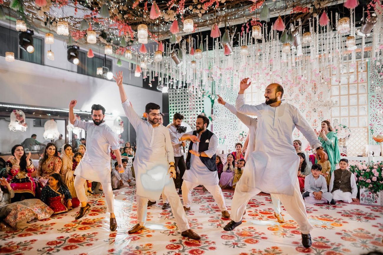 Groomsmen dancing energetically on the mehndi dance floor, guests seated and clapping around them, Mashal & Danial's wedding