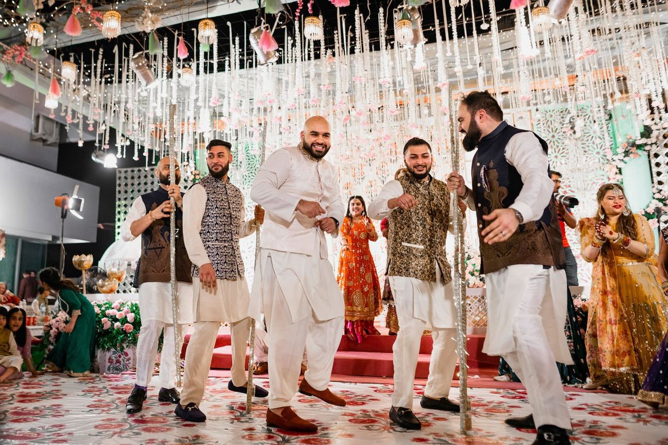 Groom dancing with friends holding decorative poles on the mehndi stage, Mashal & Danial's wedding