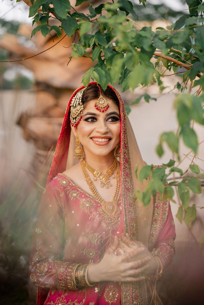 Solo bridal close-up in a pink embroidered outfit framed by tree leaves, golden hour light, Mashal & Danial's wedding