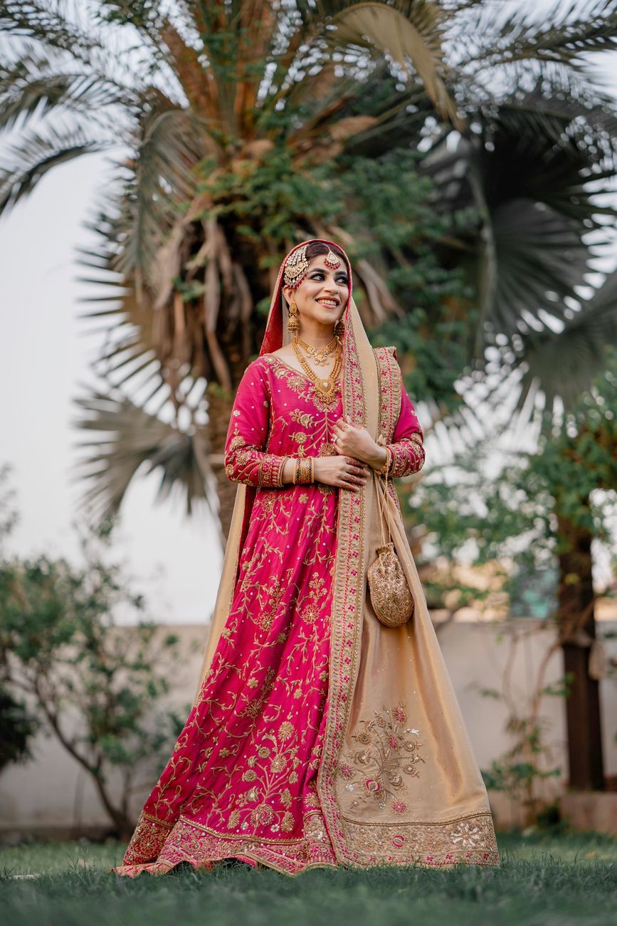 Solo bridal portrait in a pink and gold lehenga standing beneath a palm tree at golden hour, Mashal & Danial's wedding