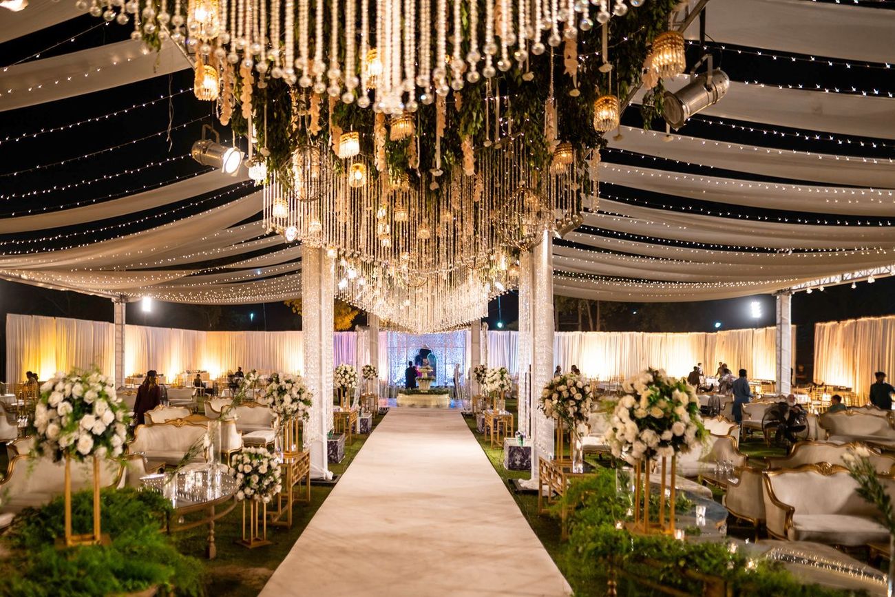 Wide shot of the empty white reception stage decorated with greenery and crystal chandeliers, Mashal & Danial's wedding