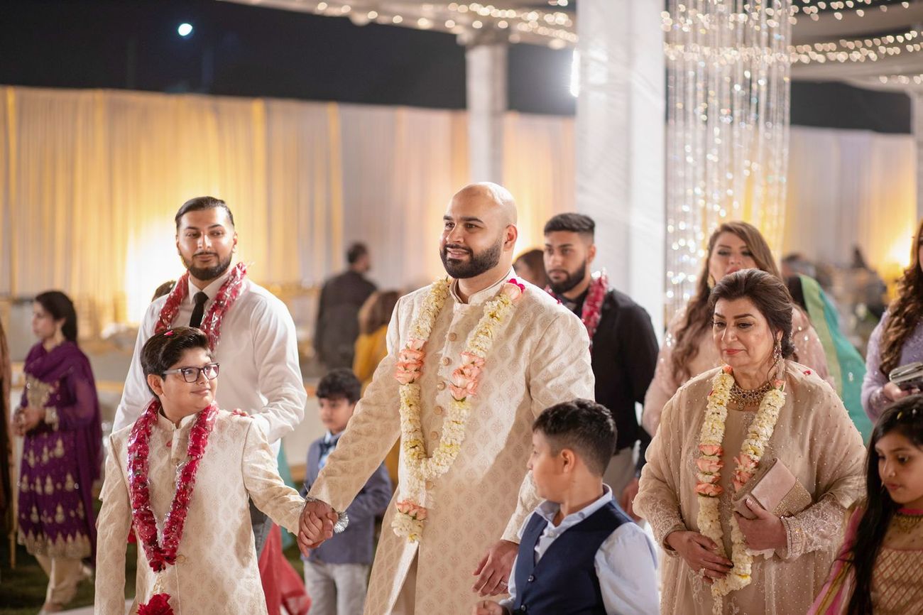 Groom walking through the reception with family members wearing flower garlands, Mashal & Danial's wedding