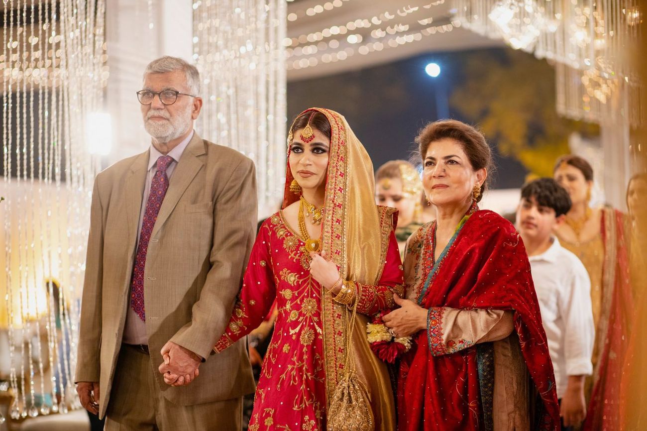 Bride's reception entrance with her parents, dressed in a red and gold lehenga, Mashal & Danial's wedding