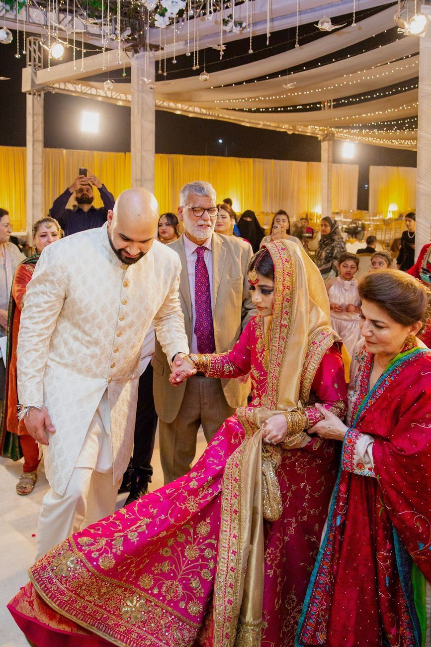 Groom helping the bride down the steps at the reception, her pink and gold lehenga train flowing, Mashal & Danial's wedding