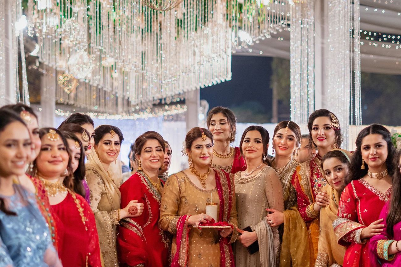 Group of women friends posing together beneath crystal chandeliers at the reception, Mashal & Danial's wedding