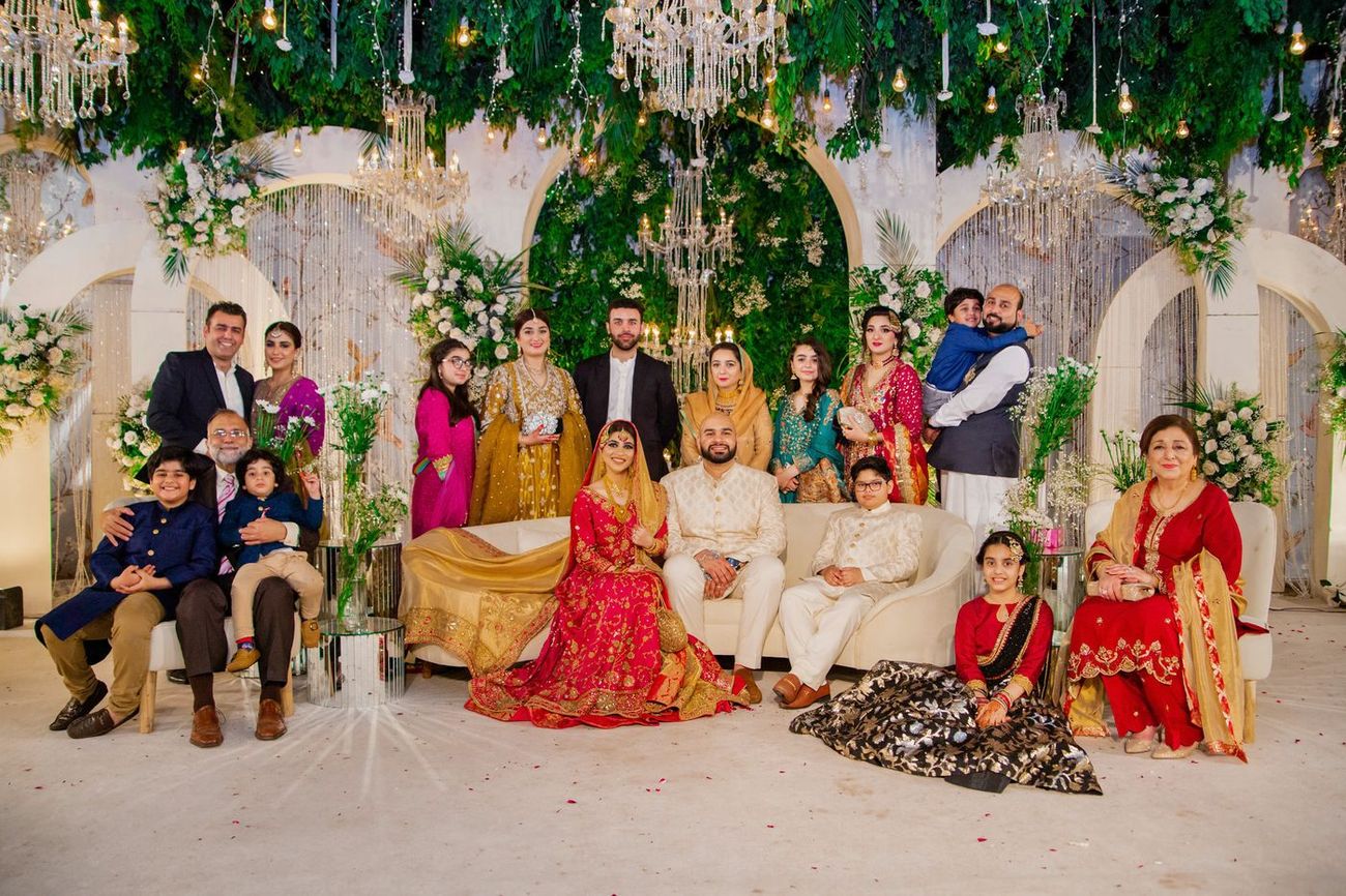 Massive extended family group portrait on the reception stage beneath arches and greenery, Mashal & Danial's wedding