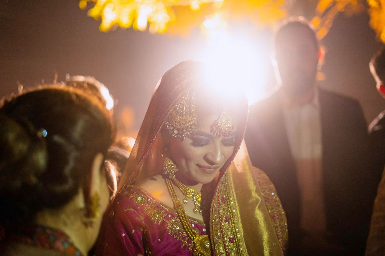 Backlit close-up of the bride smiling at the reception, golden light flaring behind her, Mashal & Danial's wedding