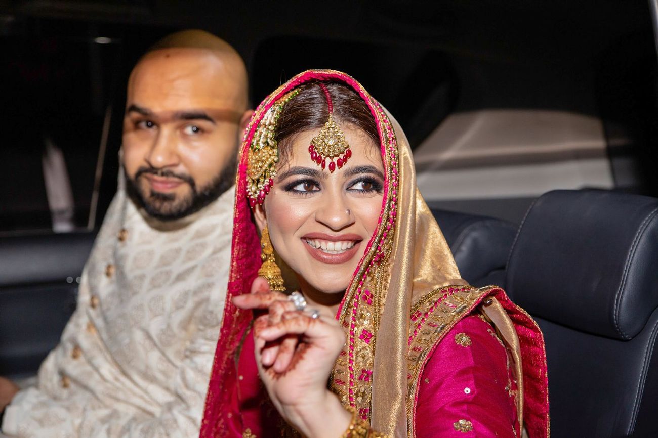 Bride and groom in the back of a car at night, bride glancing back and smiling, Mashal & Danial's wedding