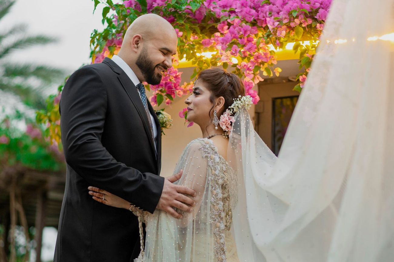 Close-up of bride and groom smiling at each other beneath a pink bougainvillea-covered roof, Mashal & Danial's wedding