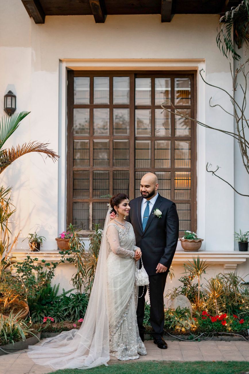 Bride and groom standing together in front of a large wooden-framed window at the residence, Mashal & Danial's wedding