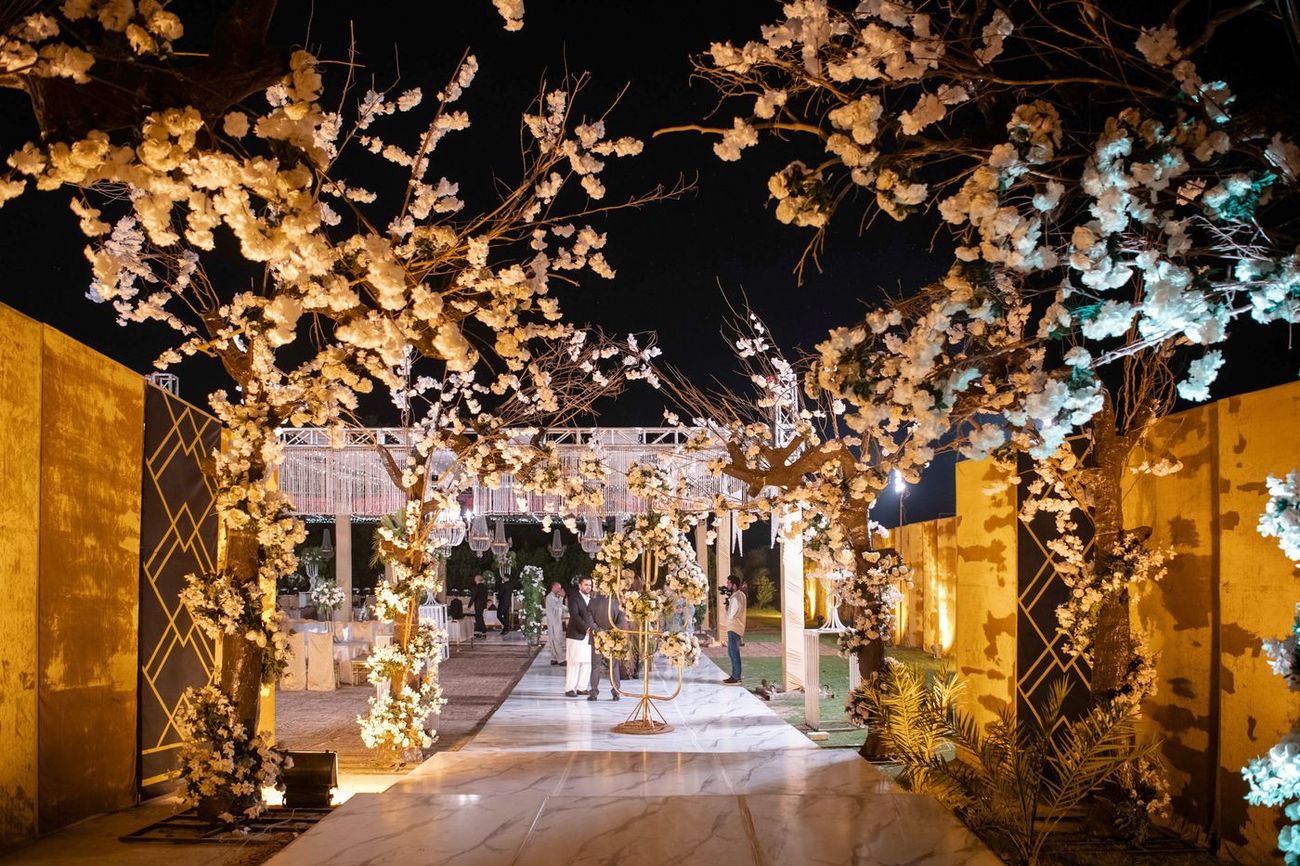 Wide night shot of the walima venue's cherry-blossom-lit walkway leading to the reception stage, Mashal & Danial's wedding