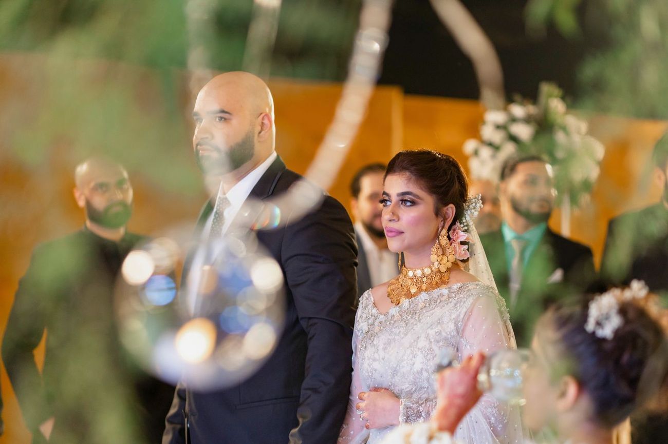 Bride and groom standing together at the walima, bride wearing a dramatic gold coin necklace, Mashal & Danial's wedding