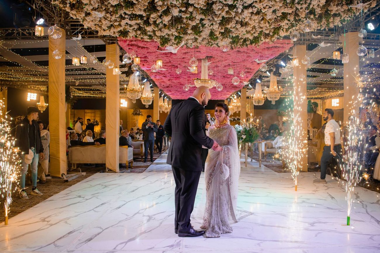 Bride and groom holding hands on the walima dance floor as cold-spark fireworks shoot up around them, Mashal & Danial's wedding