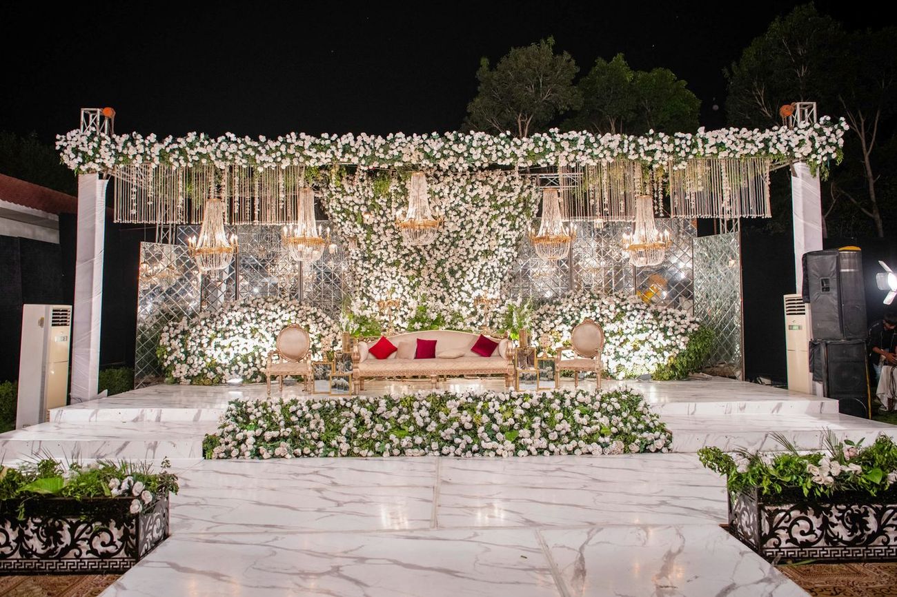 Wide shot of the walima stage decorated with white roses and crystal chandeliers at night, Mashal & Danial's wedding