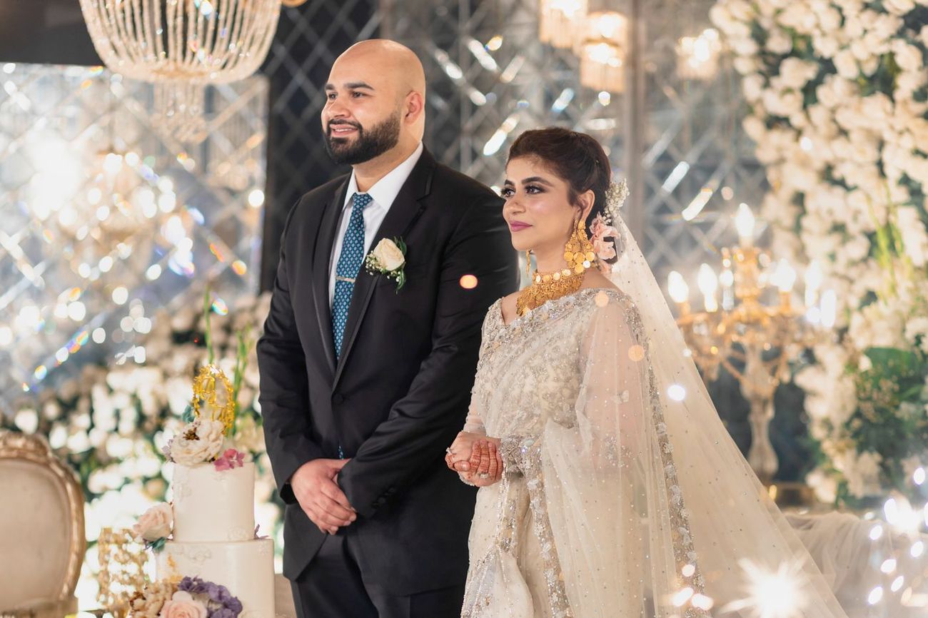 Bride and groom standing beside their wedding cake at the walima reception, Mashal & Danial's wedding