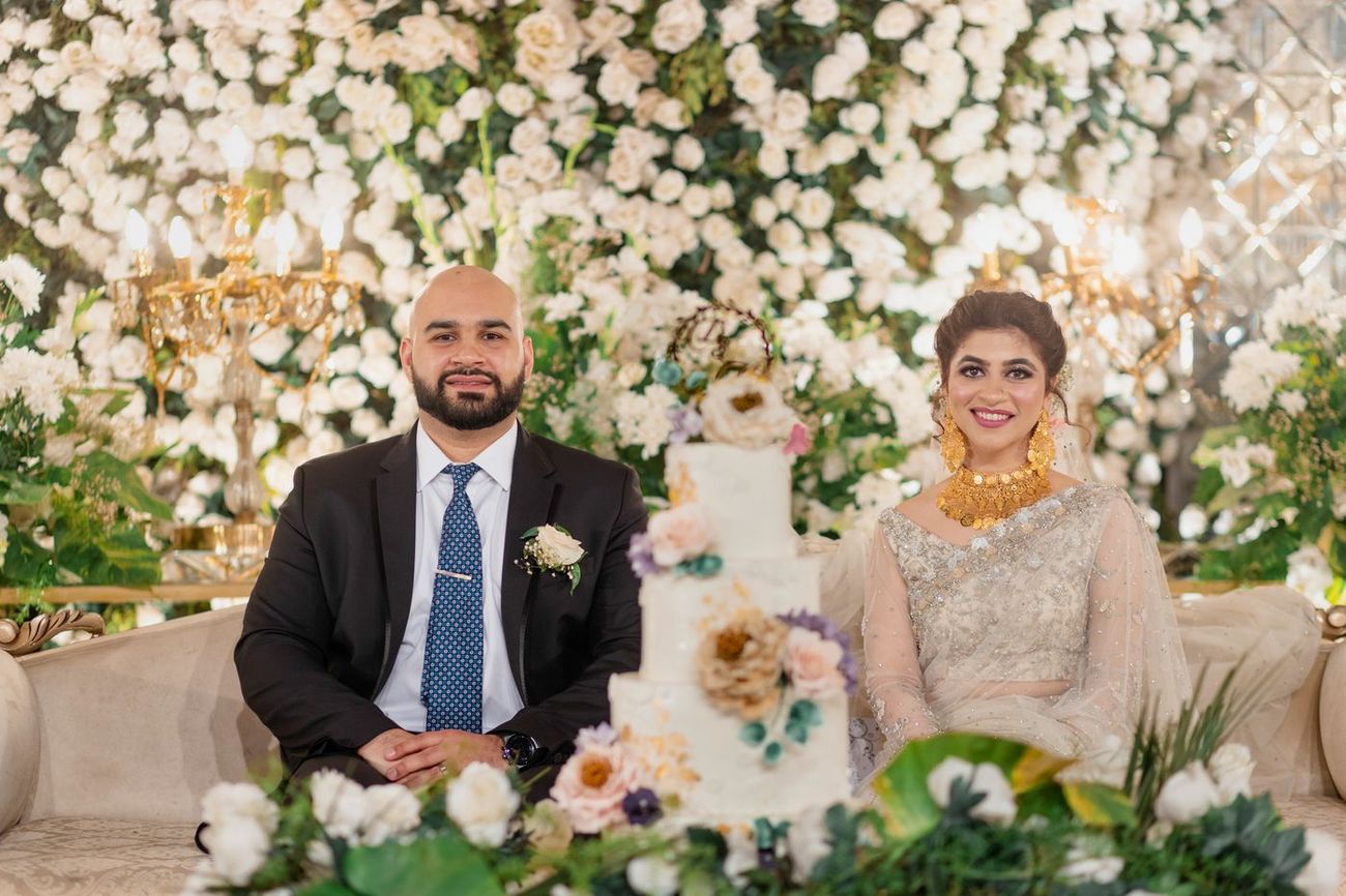 Bride and groom seated together beside their tiered wedding cake at the walima, Mashal & Danial's wedding