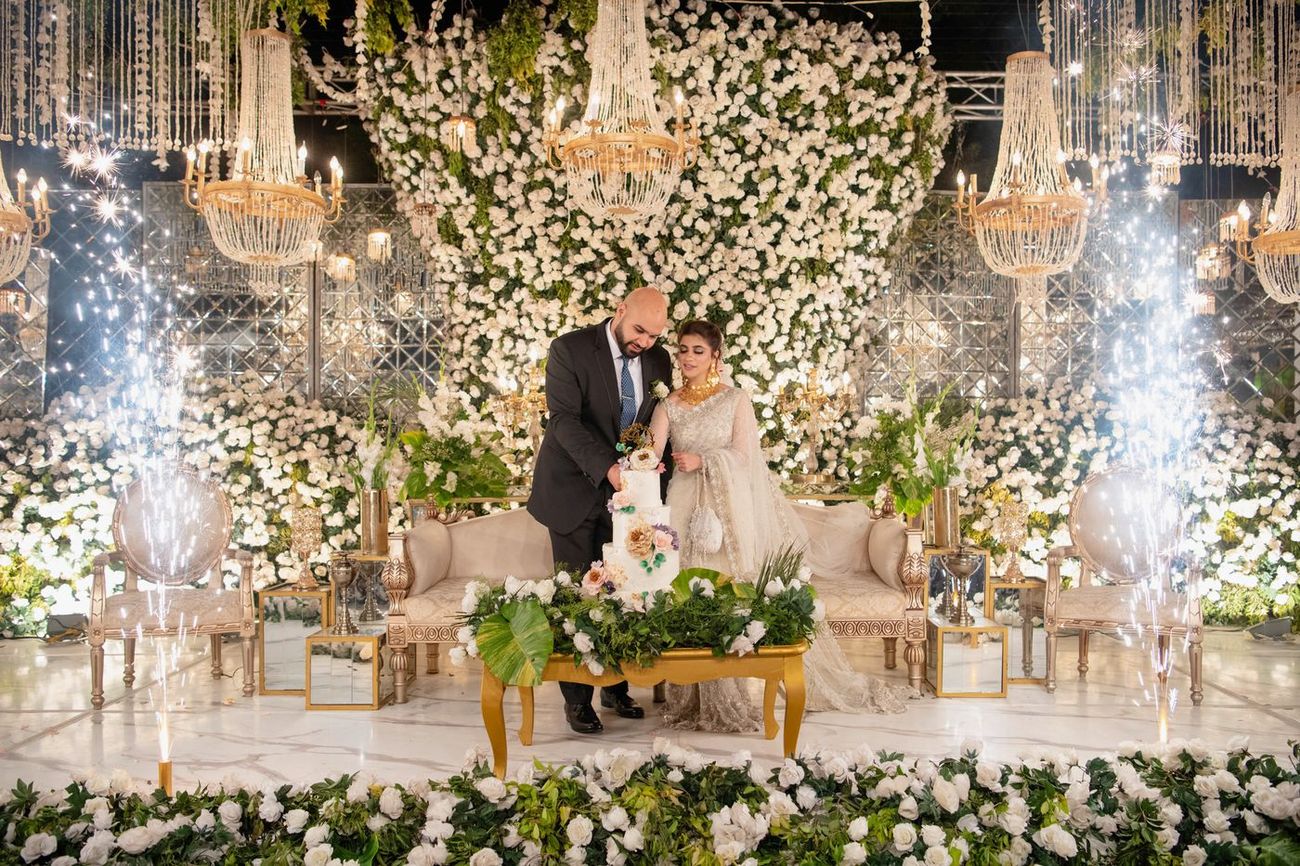 Bride and groom cutting their tiered wedding cake at the walima as cold sparks light up around the stage, Mashal & Danial's wedding