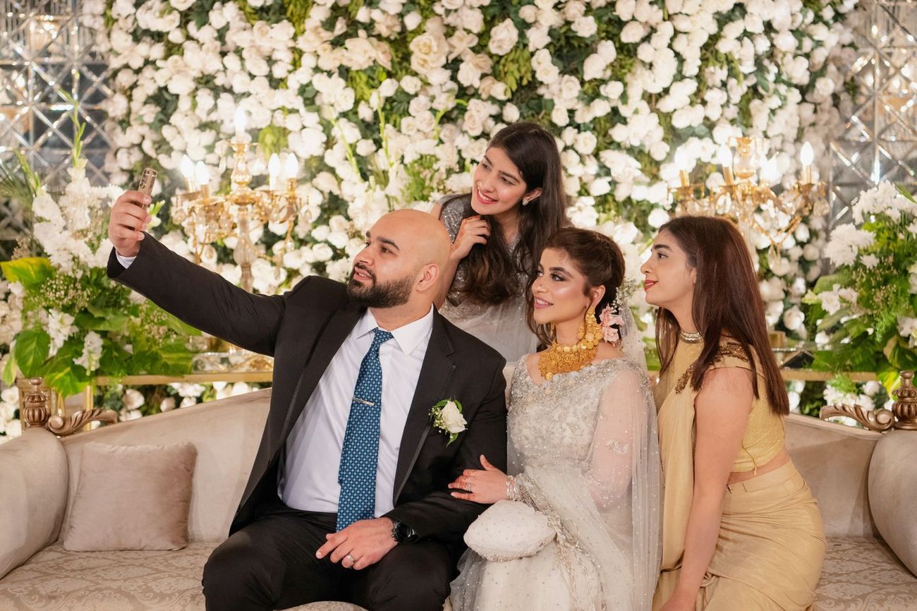 Groom taking a selfie with the bride and two friends on a sofa at the walima reception, Mashal & Danial's wedding