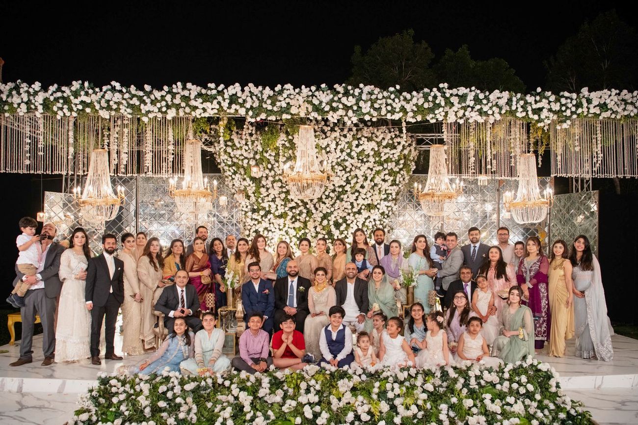 Large extended family group portrait at the walima reception beneath a floral and chandelier canopy, Mashal & Danial's wedding