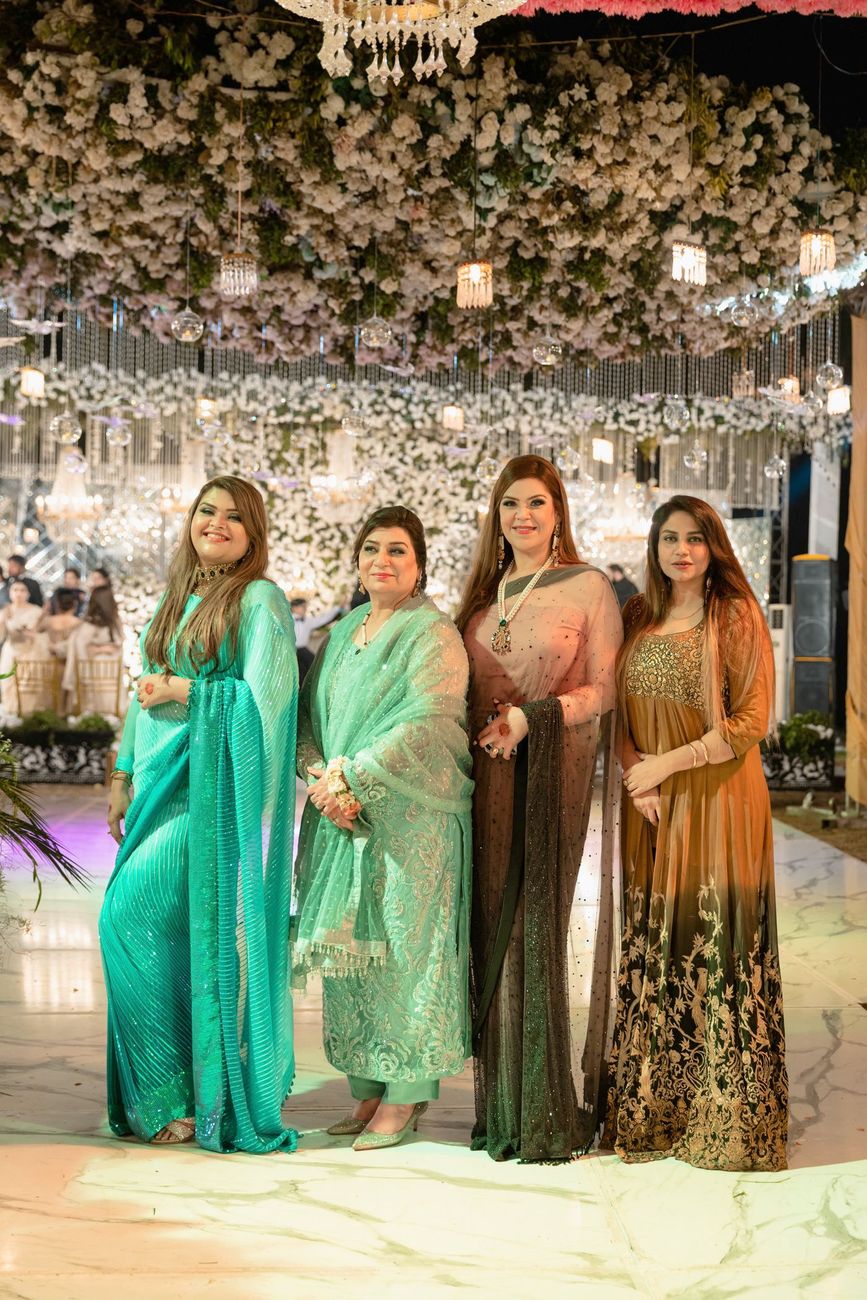 Group of four women friends posing together beneath a floral and chandelier installation at the walima, Mashal & Danial's wedding