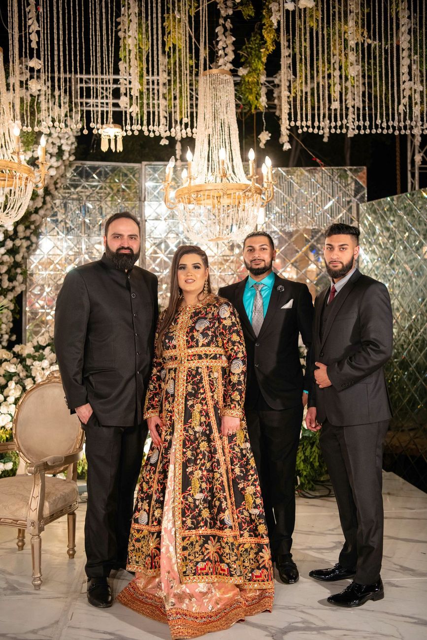 Group photo of a woman in an embellished black and gold outfit with three male friends at the reception, Mashal & Danial's wedding