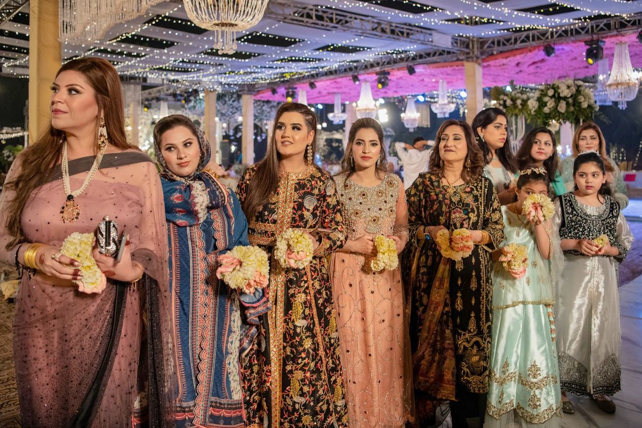 Group of women holding flower garlands posing together at the walima reception under string lights, Mashal & Danial's wedding