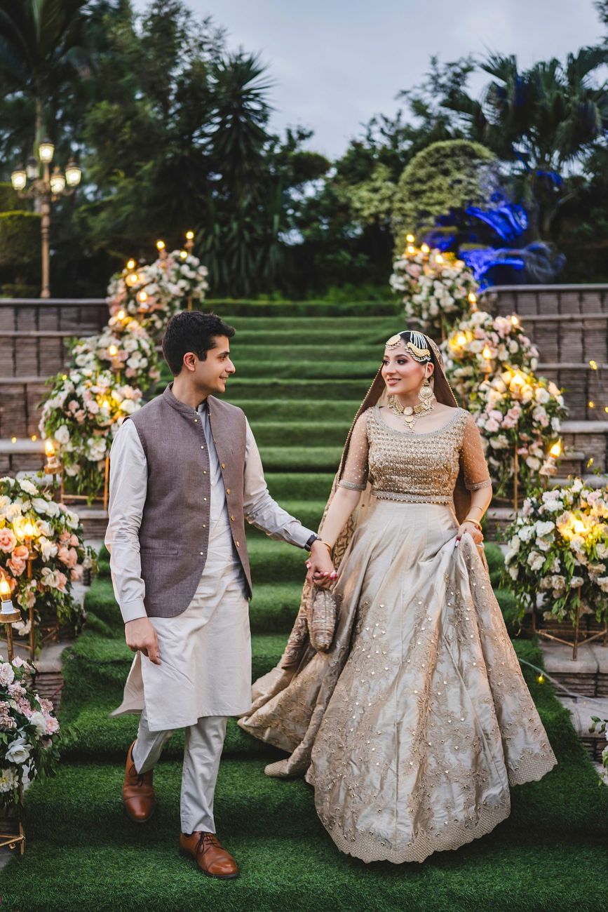 Bride and groom walking down the floral-lined grass staircase, closer view, Nayha & Rafay's wedding in Islamabad