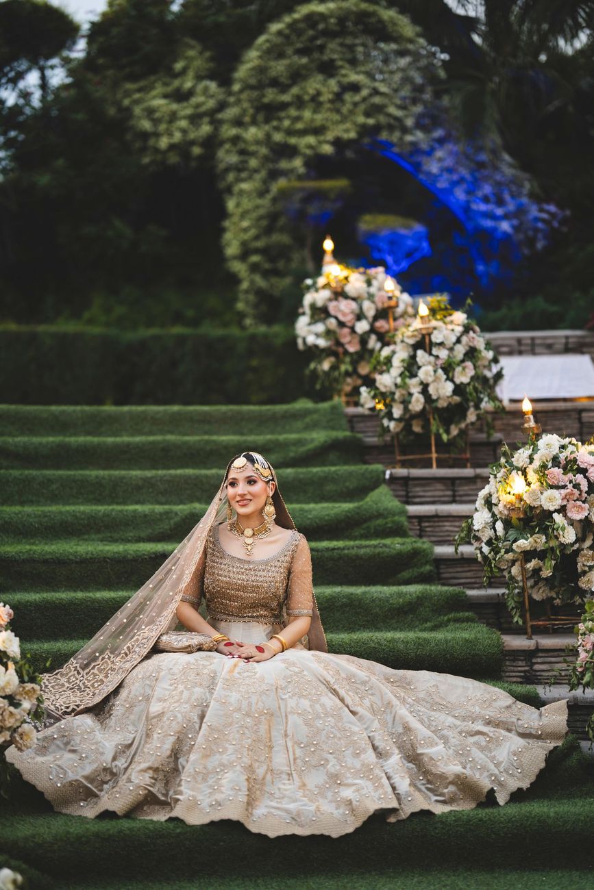 Solo bridal portrait seated on the grass staircase among glowing floral arrangements at dusk, Nayha & Rafay's wedding in Islamabad