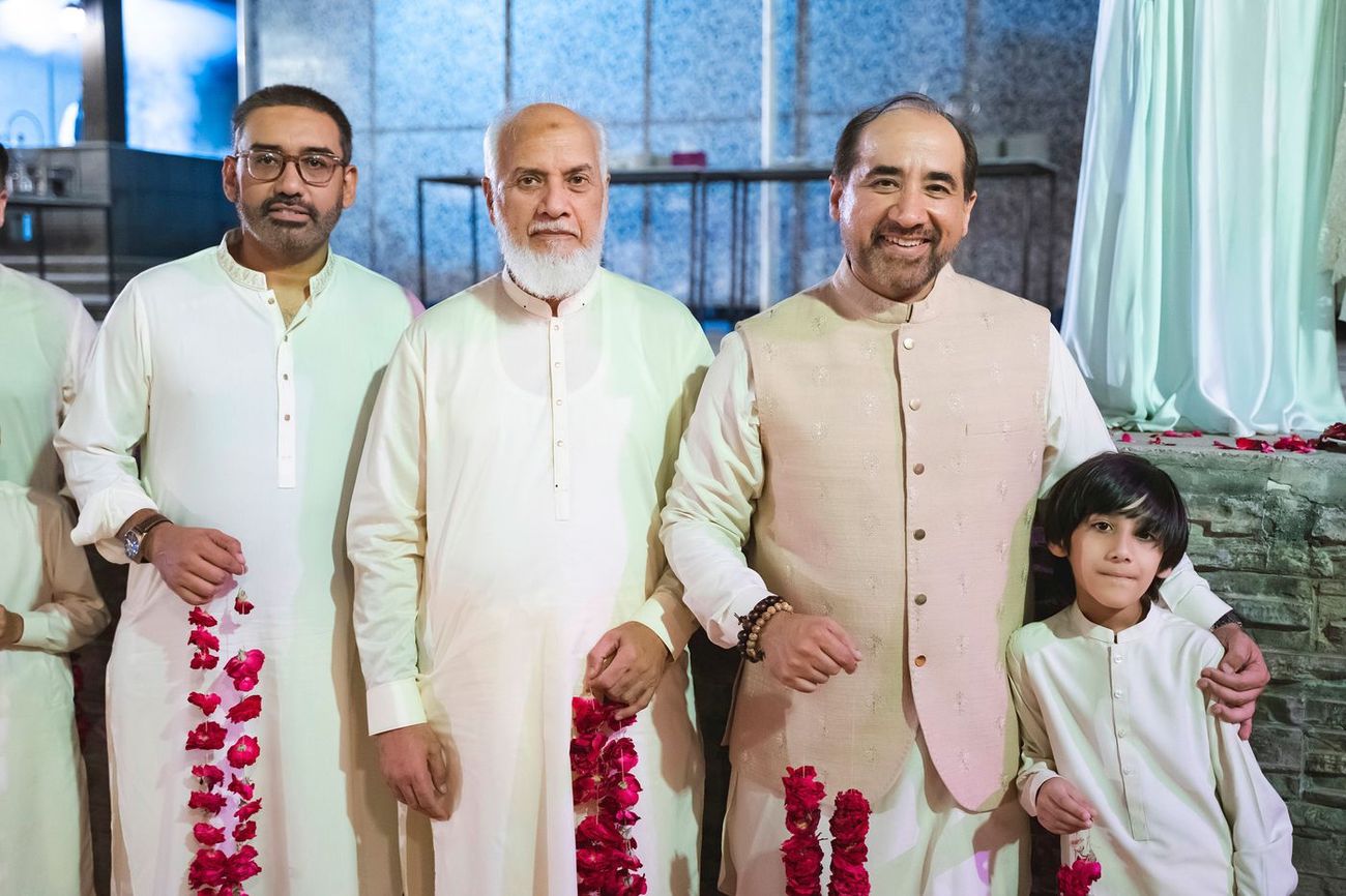 Male family members posing together holding red rose garlands ahead of the ceremony, Nayha & Rafay's wedding in Islamabad