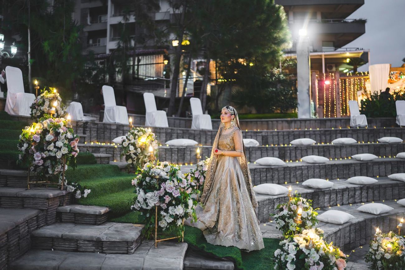 Solo bride walking down the amphitheater-style seating steps past rows of draped chairs and floor cushions, evening, Nayha & Rafay's wedding in Islamabad